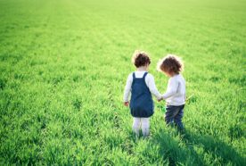 two children holding hands in a green field