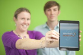 Researchers (out of focus) hold out a tablet with the mobile app loaded