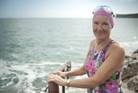 An older lady standin bu the sea in Penzance, Cornwall, in a swimming costume ready to swim in the sea