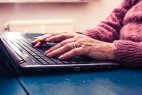 An older person's hands typing on a laptop