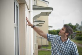 A researcher examines the outside of a house for signs of damp