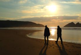 A couple walk silhouetted on the beach by a setting sun