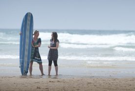 Researcher and business partenr stand on the beach with a surfboard