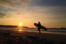 A silhouette of a surfer standing on the beach as the sun sets behind