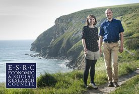 Researchers Ben Wheeler and Sarah Bell stand on a cliff face with the sea behind