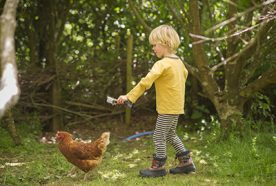 A young child films a chicken in a wooded area with a small go-pro camera