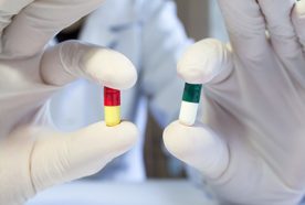 a close-up of gloved hands holding two different coloured pills