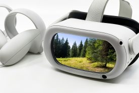 A white VR headset sits on a plain white table with a stylised view of a forest shown on its front face.