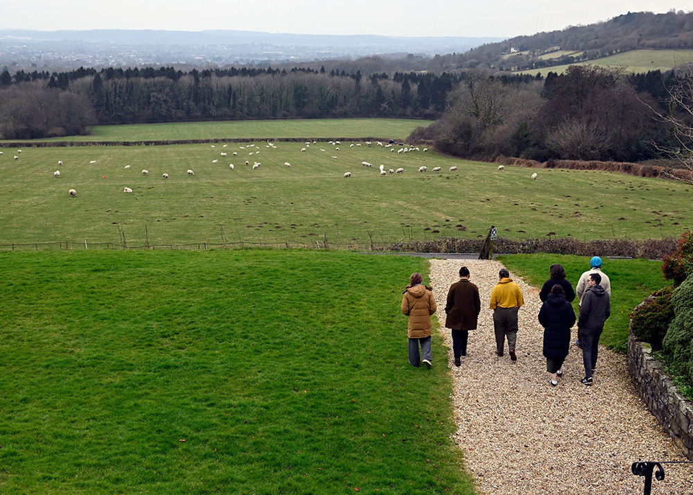 Viewed from above, a group of people walk along a gravel path towards a series of green fields. 