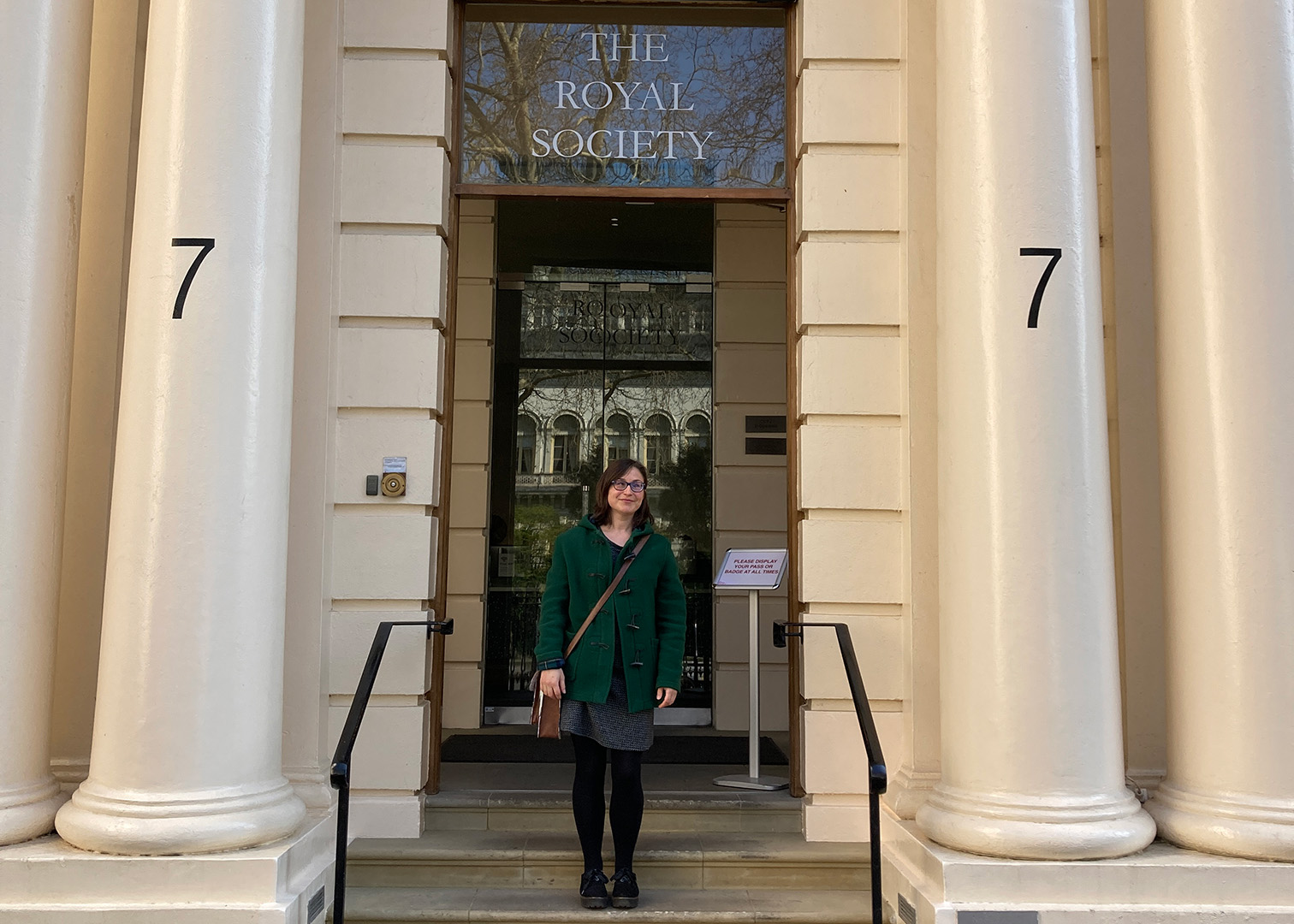 Dr Jo Garrett stands on the steps of The Royal Society building with grand columns either side.