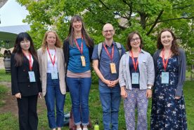 Dr Leanne Martin stands with colleagues outside the conference centre - a full length photo with green tree in the background.