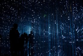 Silhouettes of people are seen in the dark through hanging points of light that mimic a data network.