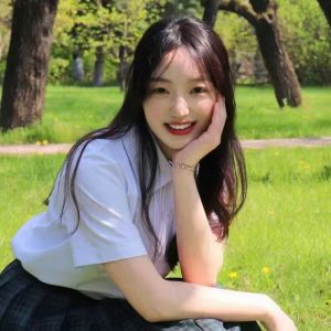 Hong Fan smiles ofr the camera in a park with trees and green grass behind.
