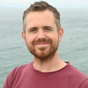 Peter smiles for the camera with a green-blue ocean in the background.
