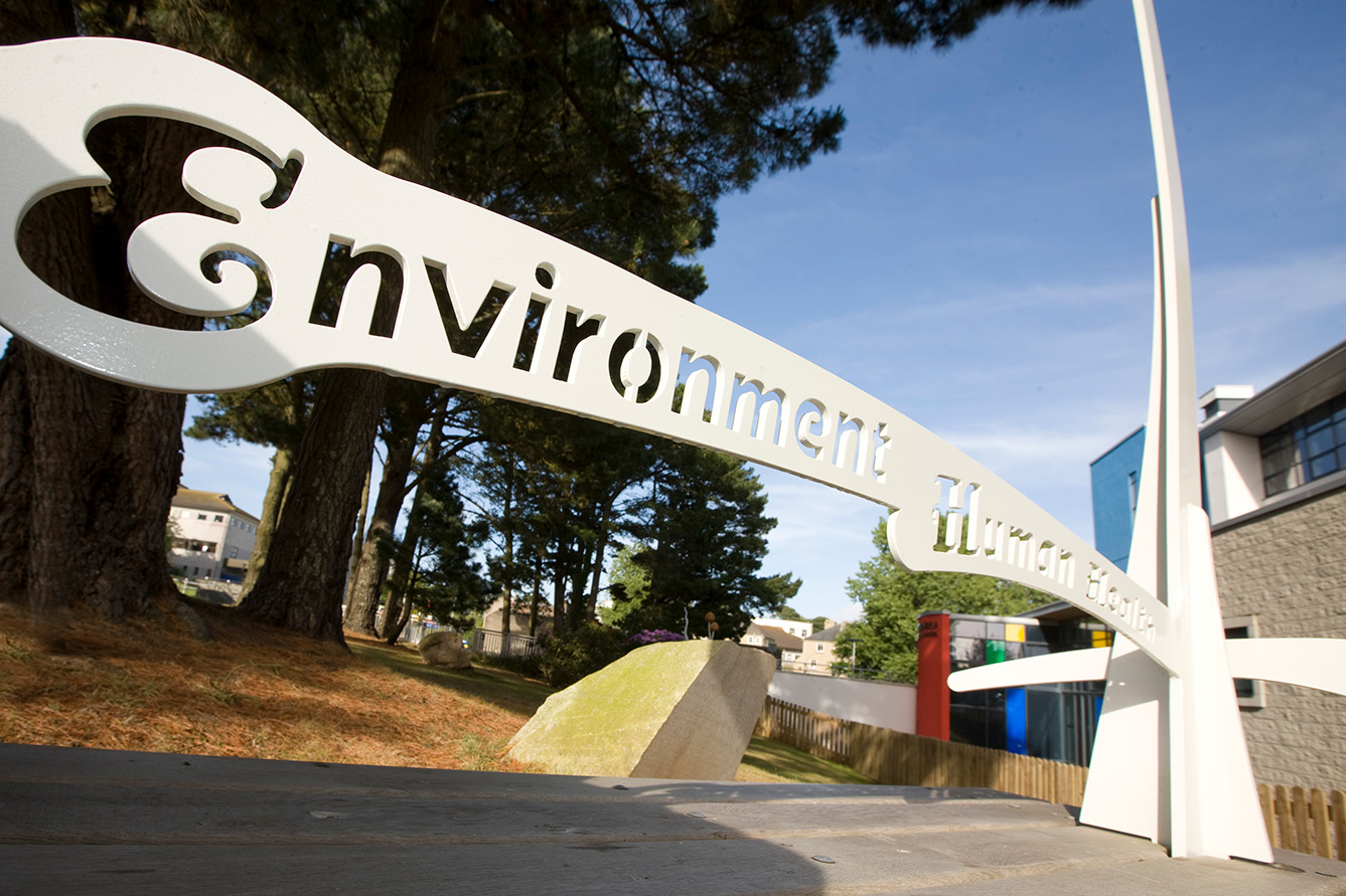 A decorative metal sculpture reads "environment human health" as it forms part of a bench seen from below on a sunny day.