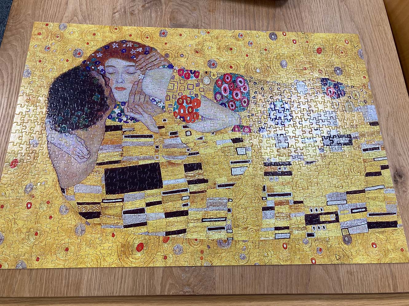 A completed puzzle of The Kiss by Gustav Klimt, showing two people embracing in a kiss on a complicated yellow background.