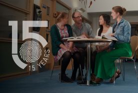 Students and their tutor sit around a table in a brightly lit atrium with the Centre's 15yr logo on the left hand side of the image.