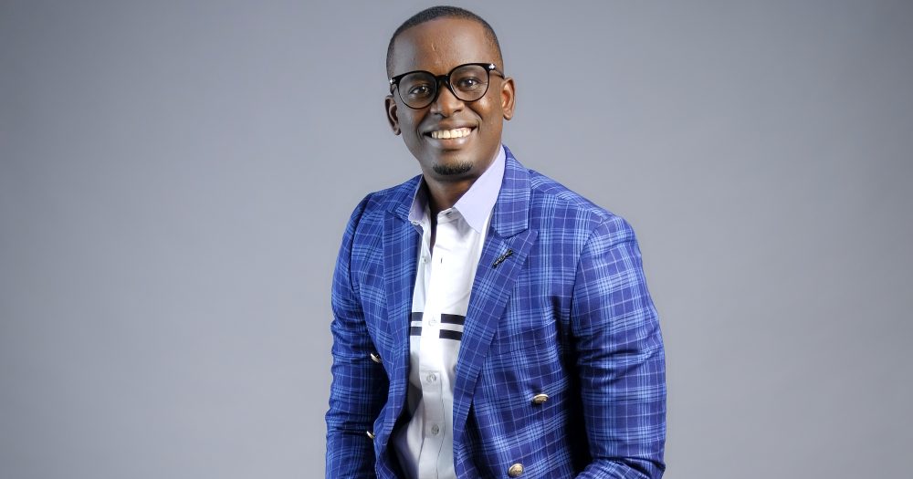 Chinonso Christian Odebeatu smiles for the camera in a photograpgy studio with grey background - he his wearing a bright blue suit.